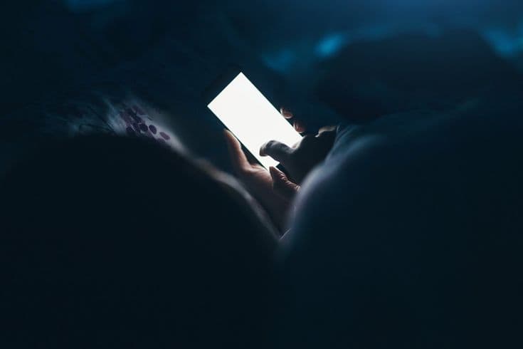 person lying awake at night, surrounded by phone screens